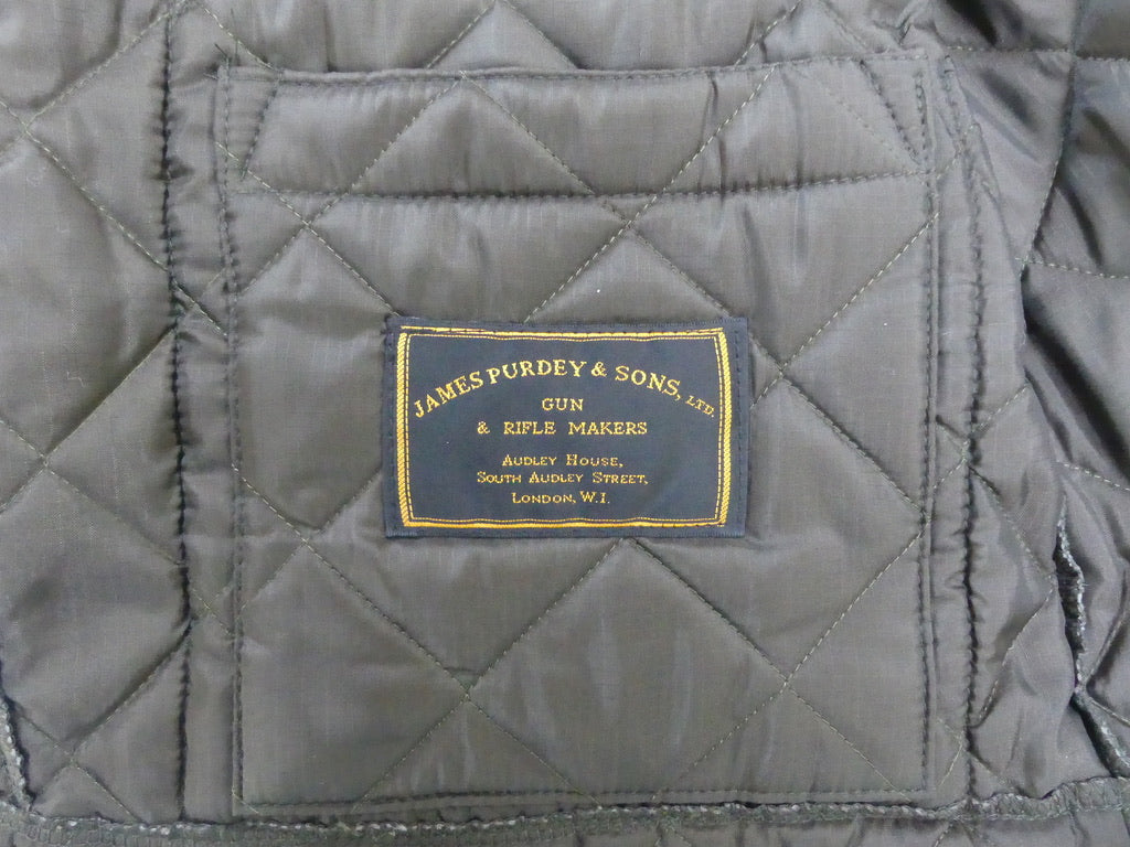 Close-up of a quilted gray fabric jacket interior with a central black brand patch reading James Purdy & Sons.
