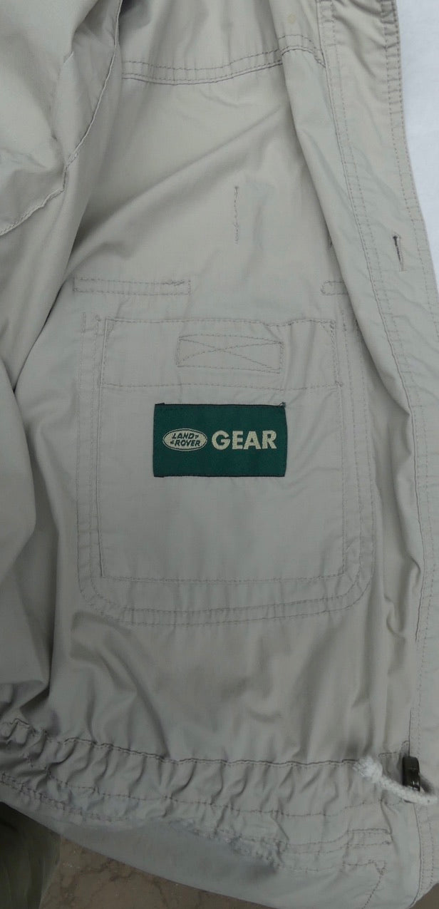 Close-up of a light beige or off-white jacket or overshirt with a green rectangular patch reading 'LAND ROVER GEAR' on the chest pocket.