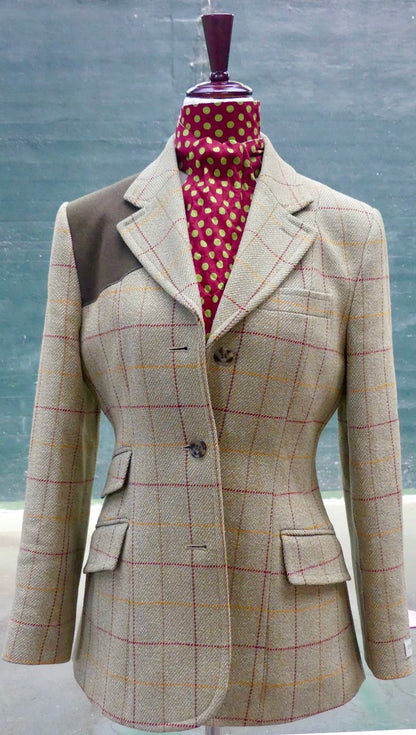 A tailored blazer displayed on a mannequin torso, featuring a beige and brown windowpane check pattern with red and yellow lines, contrast brown shoulder panels, and a red polka-dot neck scarf.