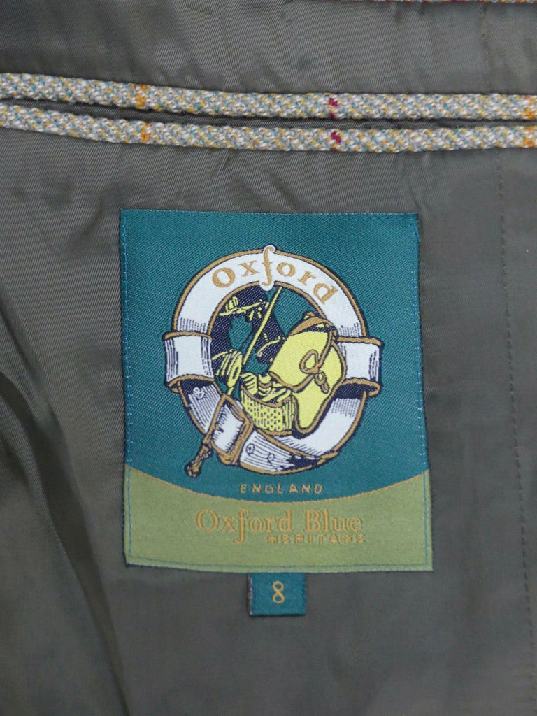 Close-up of an Oxford Blue brand fabric label sewn onto the inside of a gray garment, with a teal and green patch showing the Oxford crest and the text 'Oxford Blue England'.