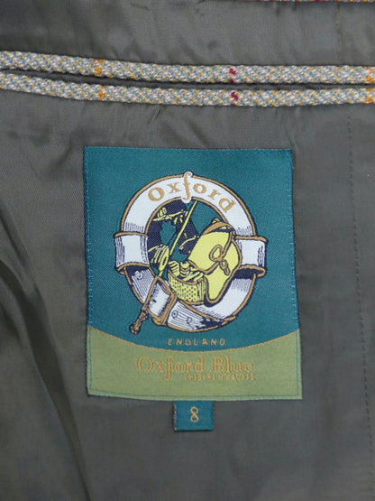 Close-up of an Oxford Blue brand fabric label sewn onto the inside of a gray garment, with a teal and green patch showing the Oxford crest and the text 'Oxford Blue England'.