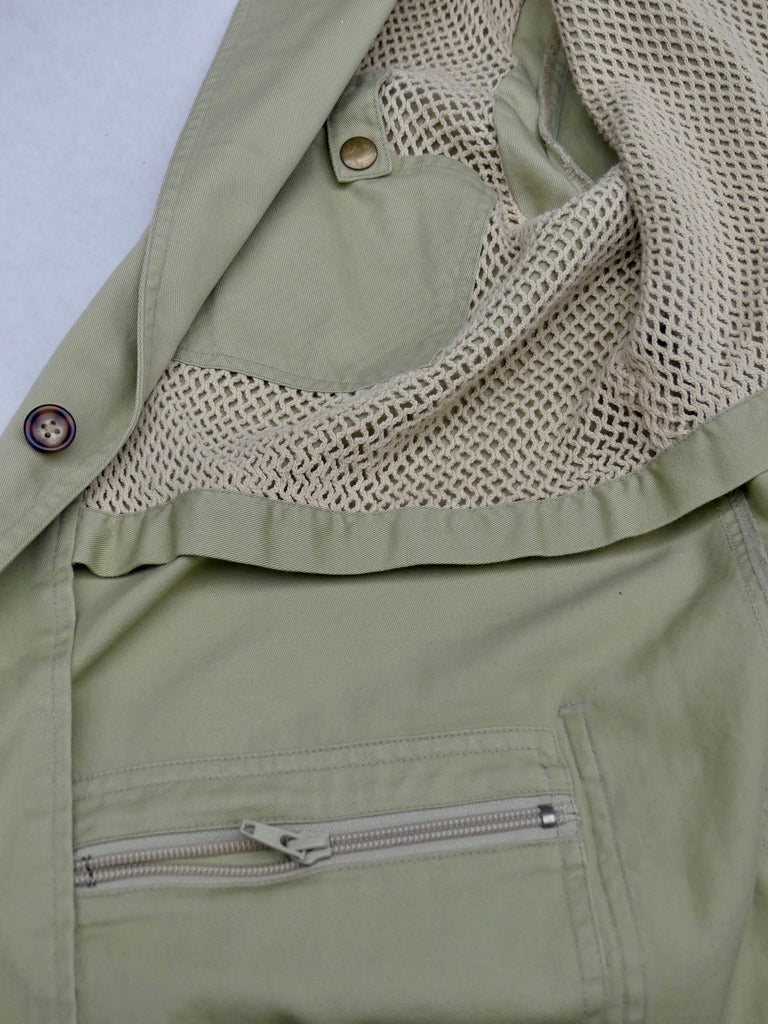 Close-up of an olive green utility jacket with a beige mesh lining and a zippered pocket.