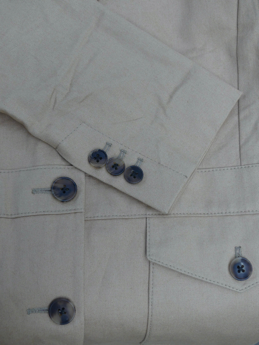 Close-up of a light beige or off-white linen shirt with dark blue buttons on the pocket flap and cuff.
