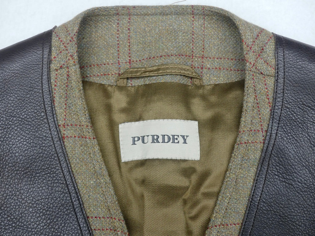 Close-up of a Purdey jacket showing the interior collar with a brown and red plaid tweed lining, olive green satin inner lining, and a white brand label.