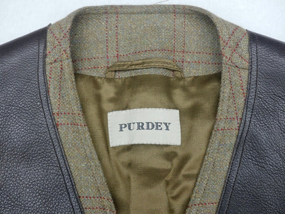 Close-up of a Purdey jacket showing the interior collar with a brown and red plaid tweed lining, olive green satin inner lining, and a white brand label.