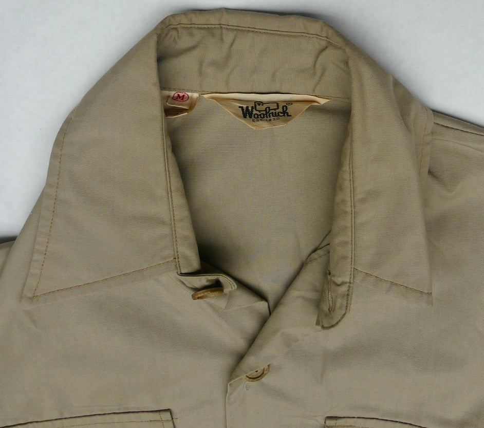 A close-up of a khaki beige button-up shirt collar, showing the interior neck label which reads 'Woolrich'