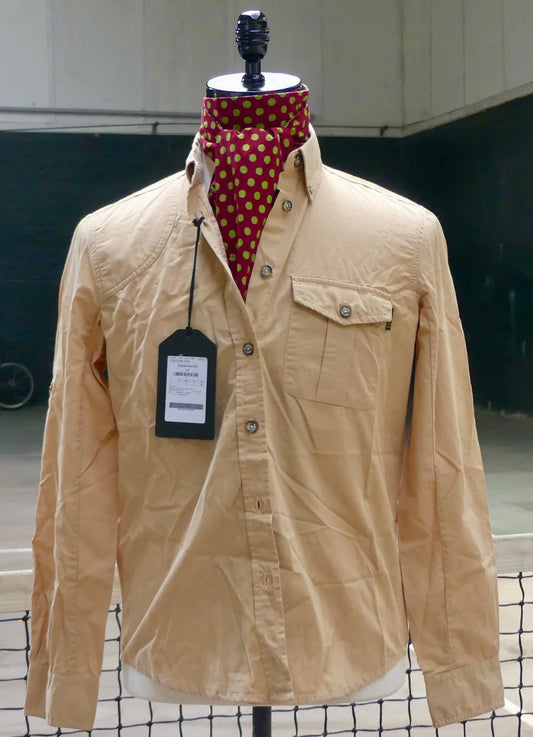 A beige long-sleeve button-up shirt displayed on a mannequin torso, styled with a red and gold polka dot neck scarf. The shirt features a chest pocket with a snap button and a black hangtag attached.