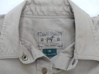 Close-up of a light beige Ralph Lauren button-down shirt collar, showing the brand label with a horse logo and a green size tag marked M.